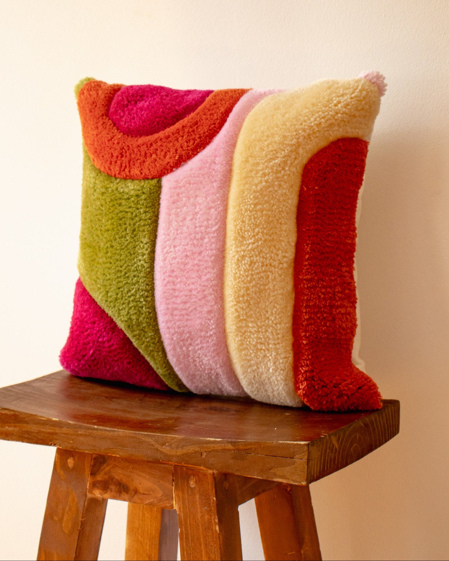 Colorful textured pillow on a wooden stool against a beige background
