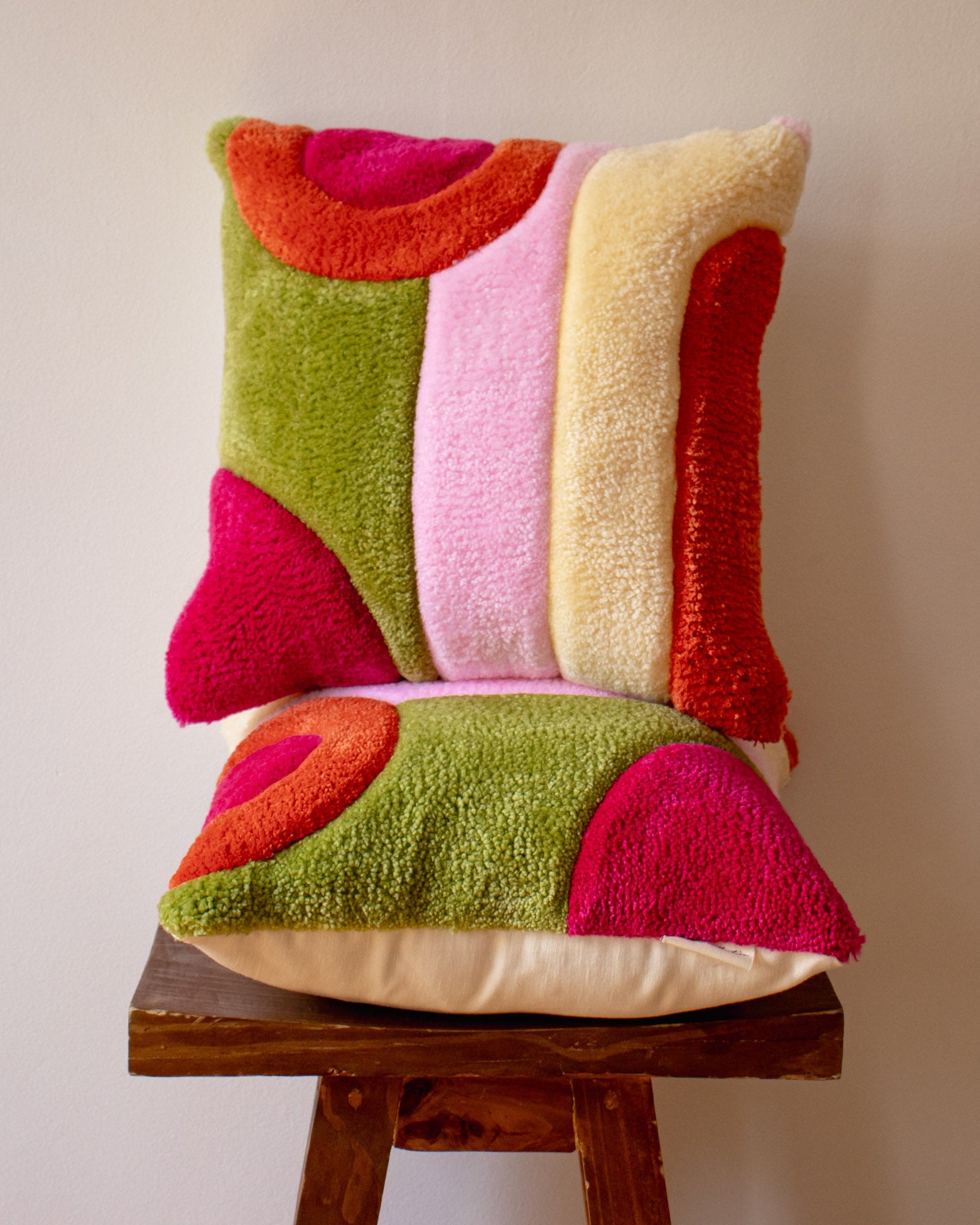 Colorful tufted pillow on a wooden stool against a plain background