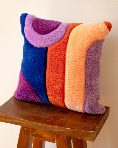 Colorful textured pillow on a wooden stool against a plain background