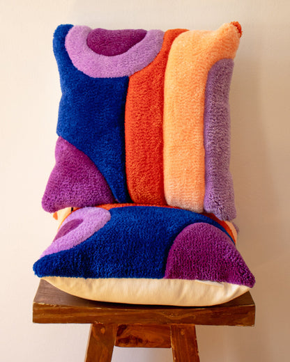 Colorful textured pillow on a wooden stool against a beige wall