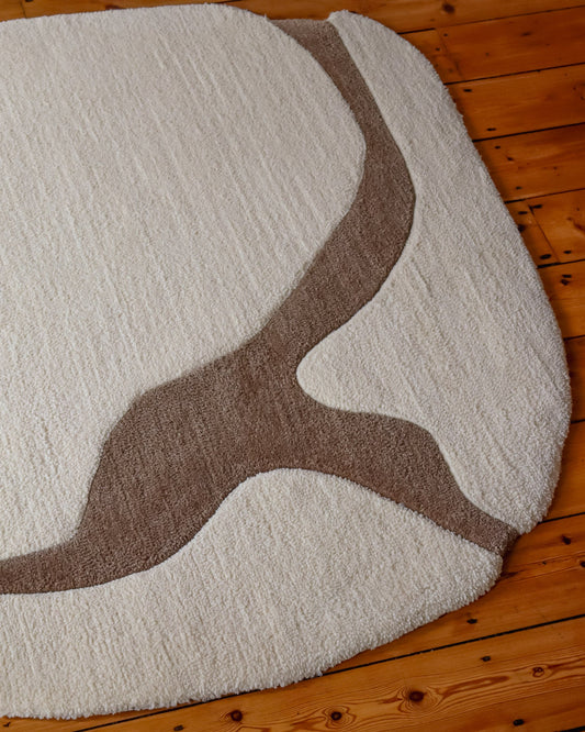 Round white rug with brown abstract design on a wooden floor