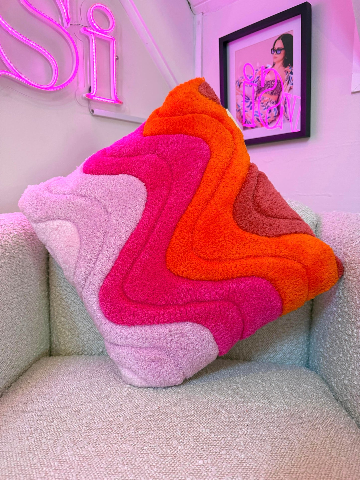 Colorful, wavy-patterned pillow on a couch with a neon sign and framed picture in the background.
